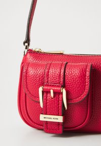 Red textured leather handbag with gold hardware, featuring a buckle detail and a zipper closure. The strap is black, providing contrast.