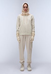 Beige hoodie met een hoge nek en drawstrings, gecombineerd met bijpassende tapered pants en gebreide handschoenen, allemaal in zachte, gestructureerde stof.