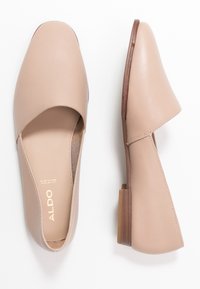 Chaussures à enfiler en cuir beige avec un bout arrondi, un petit talon carré et des côtés découpés. Design minimaliste avec des détails de surpiqûre subtils.