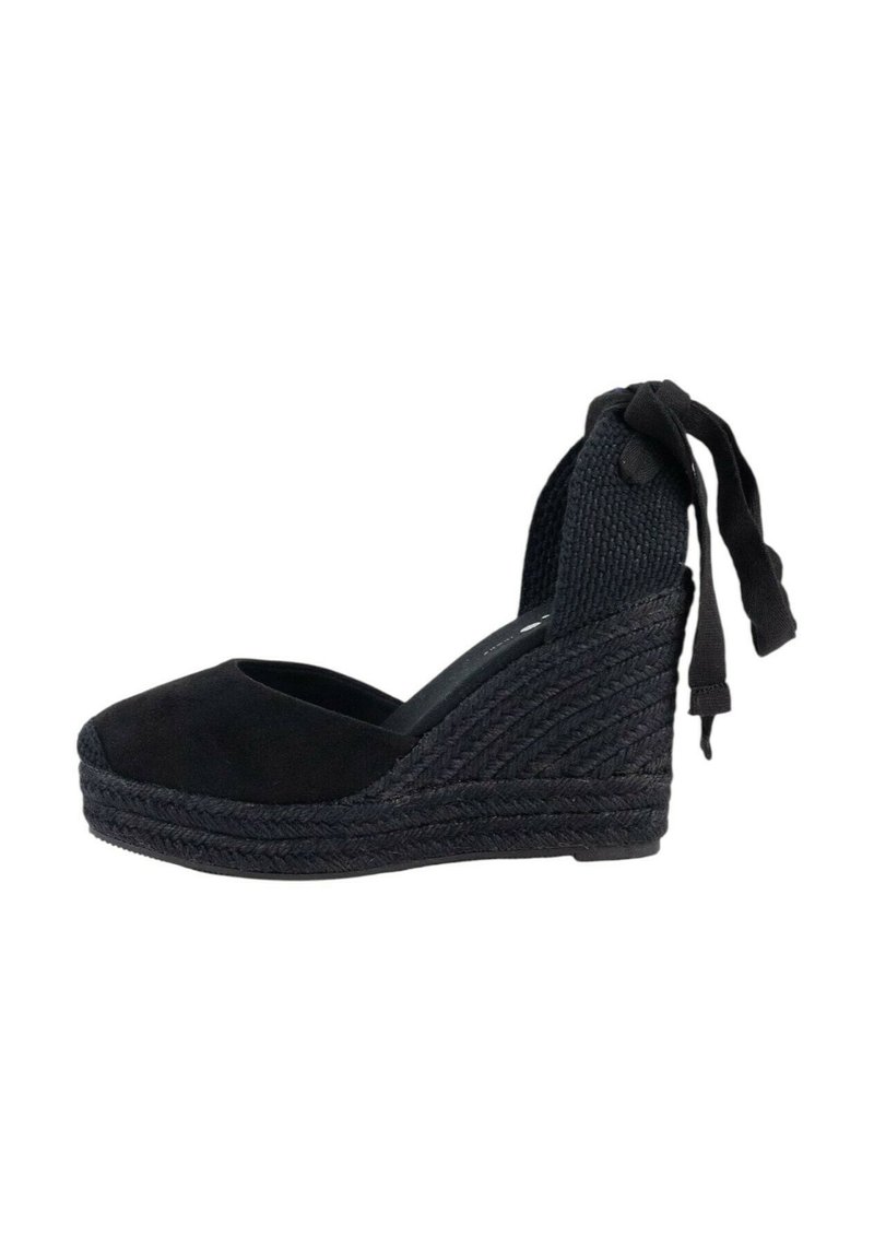 Sandalia cuña de esparto de ante negro con tacón de yute trenzado, punta abierta y una correa de tobillo tejida con lazos. Textura suave y diseño elegante.