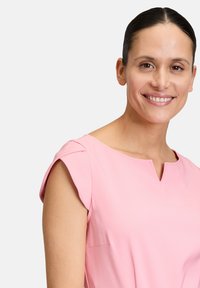 Blusa a maniche corte in tessuto rosa chiaro, con scollatura a V e dettagli sottili sulle spalle, dal texture morbido e design aderente.