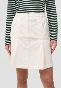 Vit kordskinnkjol med framstående veck, två sidofickor och en knappstängning i midjan, ihop med en topp i svart och vitt randigt mönster.