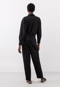 Camicia nera a maniche lunghe, con vestibilità su misura e una texture liscia, abbinata a pantaloni neri su misura con un taglio dritto.