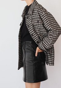 Musta-valkoinen houndstooth-kuvioitu takki, jossa on suuret napit, yhdistettynä mustaan nahkakuosisessa korkeavyötäröisessä hameessa.