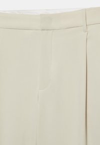 Gros plan de la taille d'un pantalon beige avec passants de ceinture, fermeture éclair avant dissimulée et texture de tissu lisse.