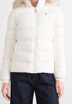 Biała kurtka puchowa z przednim zamkiem i kapturem obszytym futrem, noszona z ciemnoniebieskimi jeansami, widoczna od szyi do bioder.