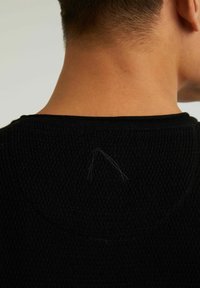 Svart stickad tröja med en texturerad mönster, rund halsringning och synliga sömdetaljer på baksidan.