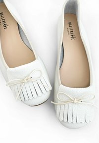Bailarinas de cuero blanco con punta redondeada, con un acabado texturizado, acentos de flecos y un lazo delgado atado en la parte delantera.