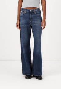 Tmavě modré kalhoty typu wide-leg vyrobené z bavlněného denimu, s vysokým pasem, klasickým pěti kapsovým designem a měděnými akcenty.