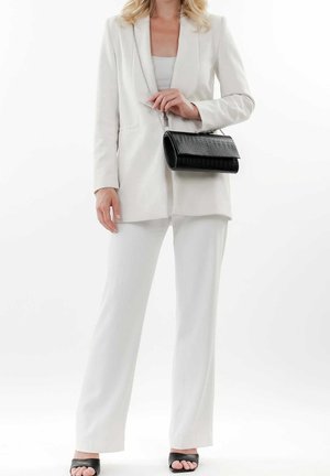 Bílý přizpůsobený blejzr přes světle šedé tričko, doplněný bílými kalhotami s širokými nohavicemi. Černá kabelka s krokodýlím vzorem a černé nazouvací sandály dotvářejí vzhled.