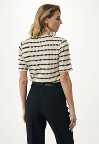Top in maglia a maniche corte con una base crema e audaci strisce zigzag nere. Abbinato a pantaloni neri a vita alta e cintura.