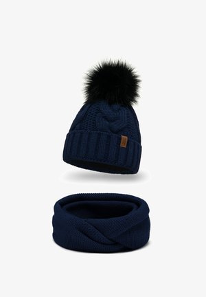 Mørkeblå strikket beanie med en faux fur pom-pom, parret med et matchende chunky strikket infinity tørklæde, begge med et struktureret mønster.