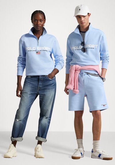 Jasnoniebieskie bluzy z kapturem na ćwierć zamka z logo "POLO SPORT", w połączeniu z przetartymi dżinsami i niebieskimi szortami. Białe sneakersy dopełniają stylizacje.