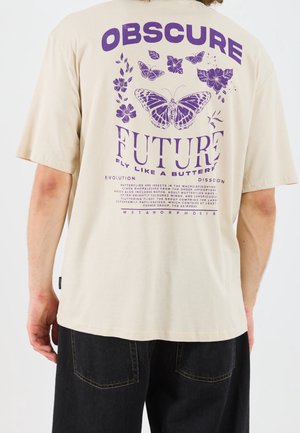 Beżowa koszulka z fioletowymi grafikami motyla i kwiatu oraz napisem "OBSCURE FUTURE fly like a butterfly" na plecach.