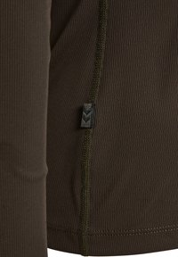 Zbliżenie ciemnobrązowej prążkowanej tkaniny z dokładnym przeszyciem i małą czarną metką z delikatnym wzorem jodełki.