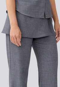 Grå skreddersydd antrekk med en teksturert topp med lagdelt kant og matchende slim-fit bukser, begge laget av et lett stoff.
