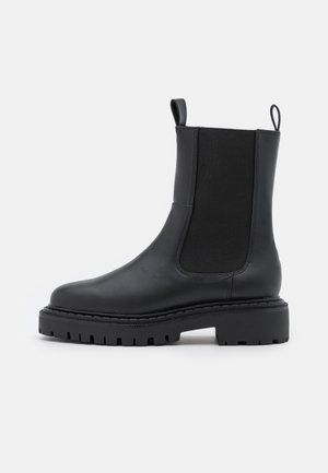 Bottes basses en cuir noir avec panneaux latéraux élastiques, semelle en caoutchouc plate et languettes pour un enfilage facile. Présentent des détails de couture discrets.