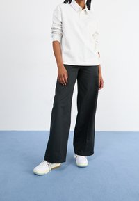 Ljusgrå långärmad polo, svarta vida byxor och vita sneakers med ljusblå sulor. Enkelt mönster, bomullsmaterial.