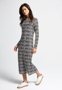 Langärmliges, grau-beiges gemustertes Kleid mit geradem Schnitt und strukturiertem Stoff, kombiniert mit weißen Sneakers, in Gehposition.