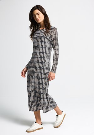 Long-sleeve, gray and beige patterned dress with a straight cut and textured fabric, paired with white sneakers, walking position.