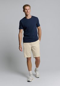 Marine blauwe T-shirt met korte mouwen, beige shorts en lichte sneakers. Materialen lijken op katoen met een gladde textuur. Eenvoudig, casual ontwerp.