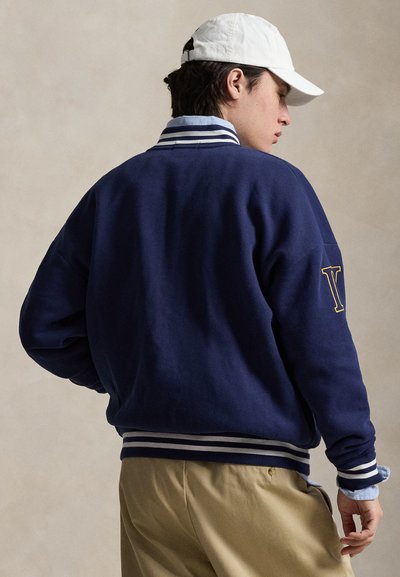 Μπλε σκούρο φούτερ με ριμπ μανσέτες και τελείωμα σε λευκές και γκρι ρίγες. Διαθέτει κίτρινο λογότυπο 'Y' στο αριστερό μανίκι. Κλασική, άνετη εφαρμογή.