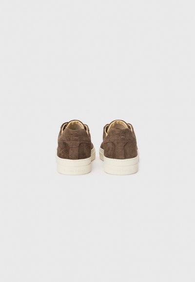 Brown suede sneakers with white rubber soles, featuring a textured upper, and a minimalist design. Back view shows stitching details.