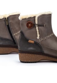 Bottines en cuir marron avec une douce doublure en fausse fourrure crème, fermeture éclair latérale et semelle texturée. Logo de la marque sur le côté.