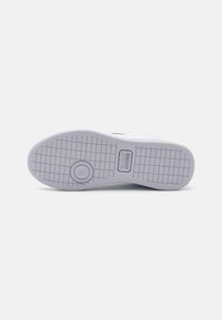 Hvit sneakersåle med en teksturert gummioverflate, med et sirkulært emblem og rutenettmønster for grep. Minimalistisk design med en glatt finish.