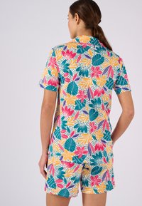 El mono de manga corta presenta un estampado vibrante con flores y hojas en tonos rosa, naranja, azul verdoso y púrpura sobre un fondo claro.