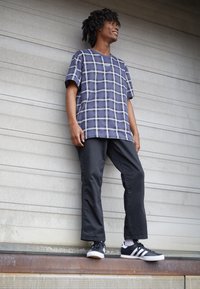 Námořnické kostkované tričko s krátkým rukávem a bílým mřížkovým vzorem, spárované s černými zúženými kalhotami a černými teniskami s bílými pruhy. Hladká textura.