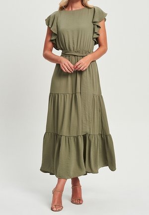 Femme portant une robe maxi olive à volants avec des manches courtes volantées et une ceinture à la taille, assortie à des talons nude à bride cheville.