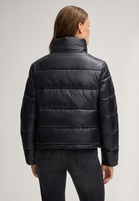 Giacca a vento nera con collo alto, design trapuntato e tessuto in nylon liscio. Presenta cerniere laterali e una vestibilità corta.