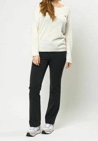 Haut à manches longues crème clair avec un petit logo, associé à un pantalon noir ajusté et des chaussures de sport gris-blanc. Texture de tissu lisse.