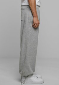 Grå afslappede sweatpants med sidelommer, elastiske manchetter og snor i kanten, parret med hvide sneakers.