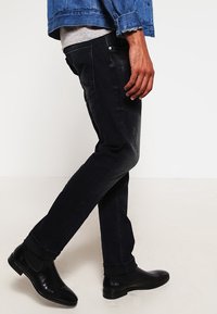 Svarta denimjeans med slim-fit design, med en blekt textur och sidofickor, parat med svarta anklar stövlar.