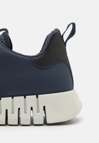 Navy leather sneaker with textured dark accents, a cushioned white sole, and a pull tab at the heel. Stitched detail along the seams.