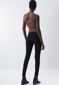 Top marrón de canalé de un solo hombro combinado con unos jeans negros ajustados. El conjunto se complementa con botas negras de tobillo con un tacón grueso.