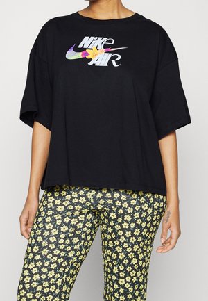 Osoba nosząca czarną, oversize koszulkę Nike Air z kolorowym kwiatowym logo oraz czarne legginsy w drobne żółte kwiatki.
