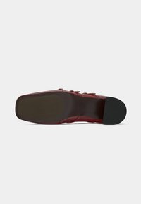 Red shoe bottom view showing a smooth rubber sole with a flat edge, subtle texture, and no visible patterns or hardware.
