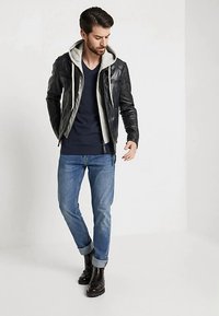 Jachetă de piele cu glugă gri, tricou bleumarin și blugi albaștri întorși la mansete, asortați cu ghete maro închis până la gleznă. Look casual, pe straturi.