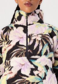 Polar z wysokim kołnierzem, z wielokolorowym kwiatowym wzorem na czarnym tle, zamkiem błyskawicznym oraz miękką, teksturowaną tkaniną.