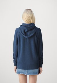 Sudadera azul marino de corte relajado, con capucha ajustable, puños y dobladillo acanalados. La vista posterior muestra un tejido suave y mangas raglán.