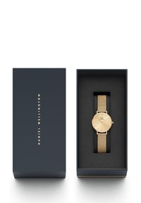 Montre à bracelet en maille dorée dans une boîte bleue marine. Cadran rond avec un visage doré et des marqueurs minimalistes. Doublure noire douce à l'intérieur de la boîte.