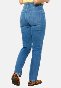 Modri denim jeans s ozkim krojem, visokim pasom in petimi žepi. Tkanina ima gladko teksturo in je kombinirana z obutvijo z leopardjim vzorcem.