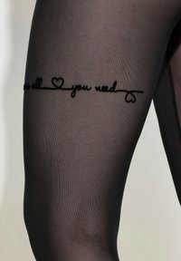 Černé průsvitné punčocháče s nápisem "All you need" a srdíčkem v oblasti stehna. Text je výrazně viditelný.