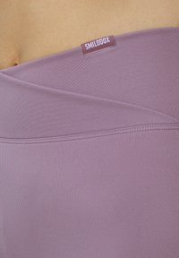 Fioletowe legginsy z wysokim stanem wykonane z gładkiego, elastycznego materiału z teksturowanym pasem i przeszyciami. Z logo na metce.