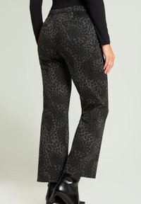 Pantalones con estampado de leopardo en negro y gris, de corte recto, con cintura media y bolsillos traseros. Combinados con botas negras de tacón.