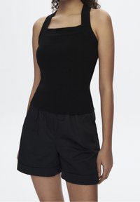 Zwarte geribbelde tanktop met een vierkante halslijn en brede schouderbanden, gecombineerd met zwarte losse shorts met omgeslagen zoom en trekkoord.