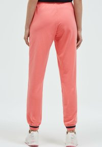 Korallenfarbene Jogginghosen aus weichem Stoff, mit elastischem Bund und gerippten Bündchen. Kombiniert mit weißen Sneakern mit dekorativen Akzenten.